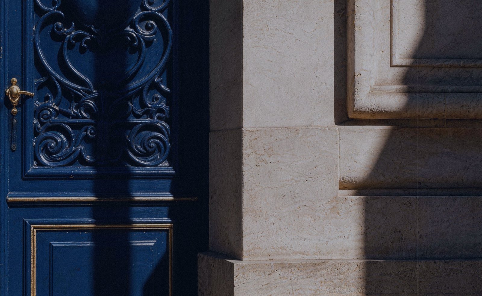 An ornate blue door and a sunlit stone facade
