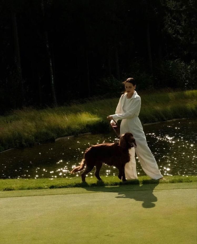 A woman walking a dog through a riverside garden